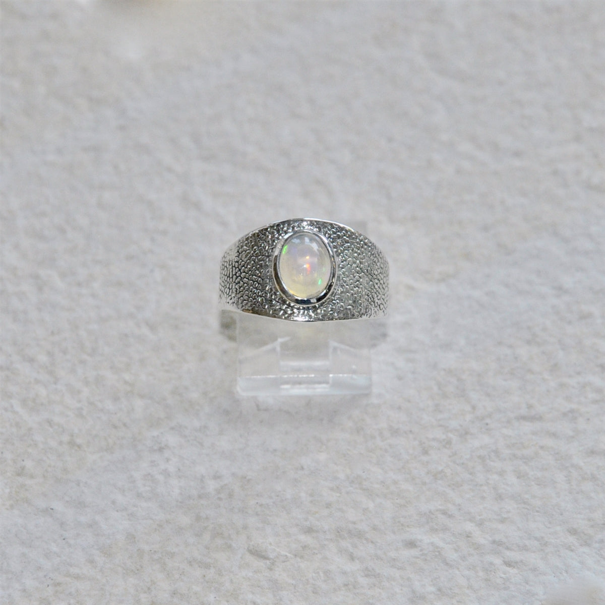 Silver ring with a central opal gemstone on a textured white background